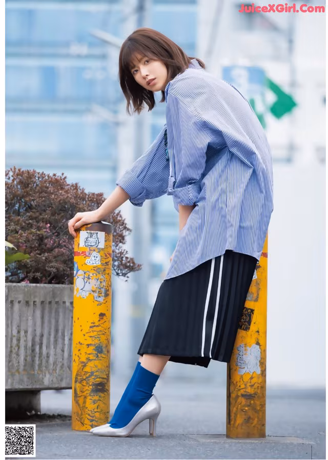 A woman leaning against a yellow pole wearing a blue and white striped shirt.
