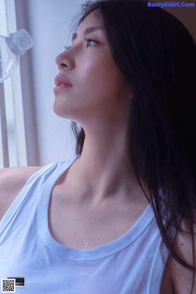 A woman in a white tank top looking out a window.