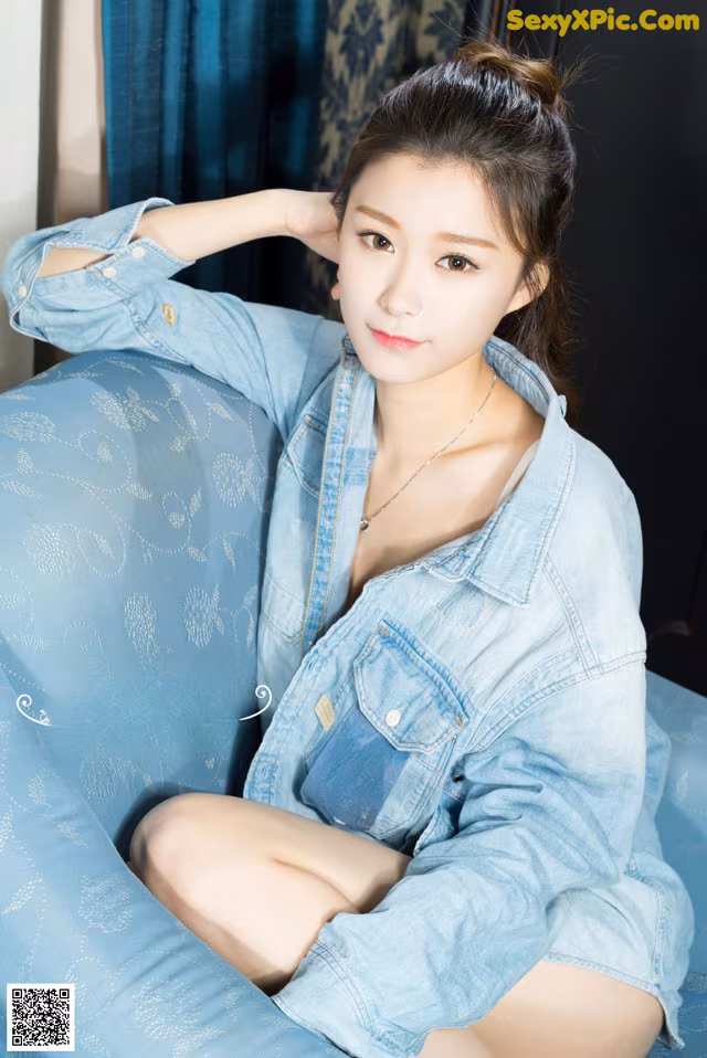 A woman sitting on a blue couch wearing a denim shirt.