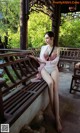 A woman sitting on a wooden bench in a pink robe.