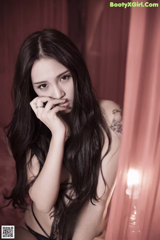 A woman with long black hair sitting on a bed.