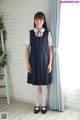 A woman in a school uniform standing in front of a window.