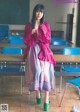 A woman standing in front of a classroom full of desks.