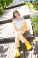 A woman sitting on a wooden deck wearing a yellow and white outfit.