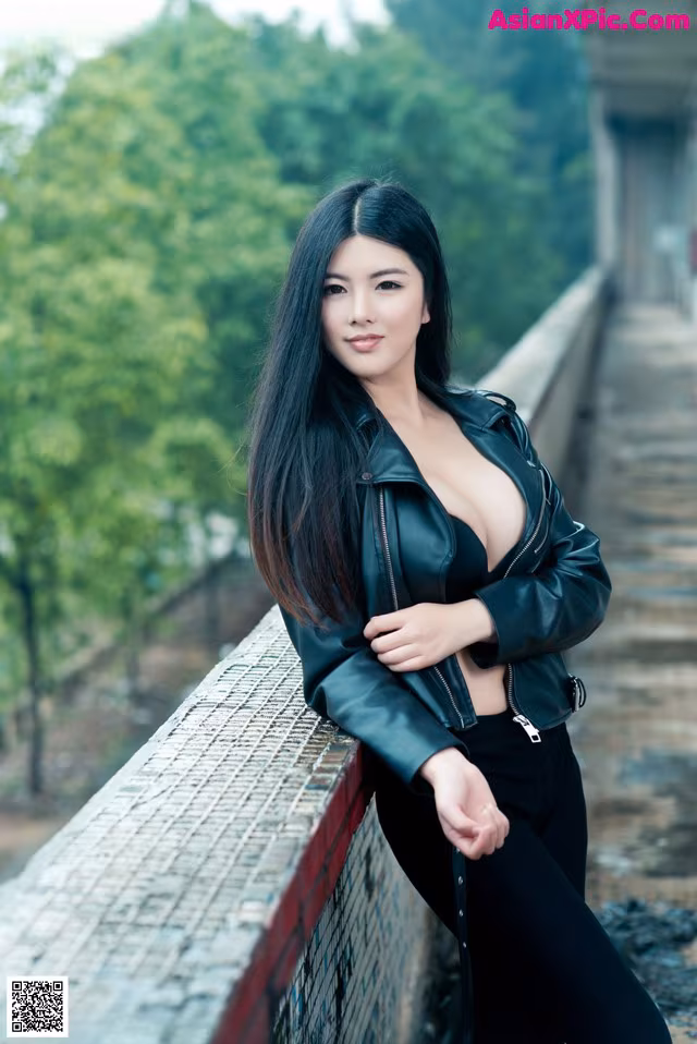 A woman in a black leather jacket leaning against a fence.