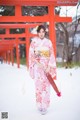 A woman in a kimono standing in front of a red torii gate.