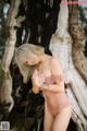 A woman in a pink bathing suit leaning against a tree.