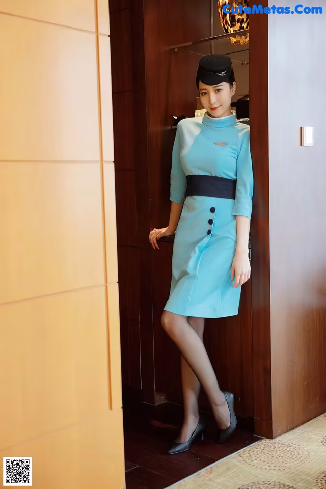 A woman in a blue dress standing in front of a door.