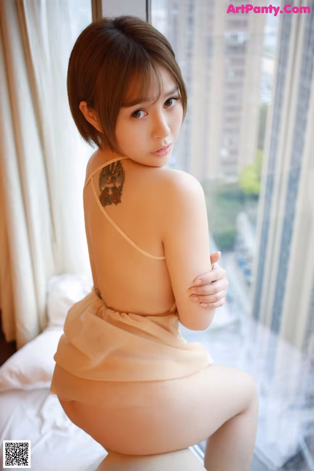 A woman sitting on top of a bed next to a window.