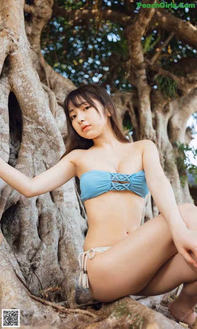 A woman in a blue bikini sitting on a tree.