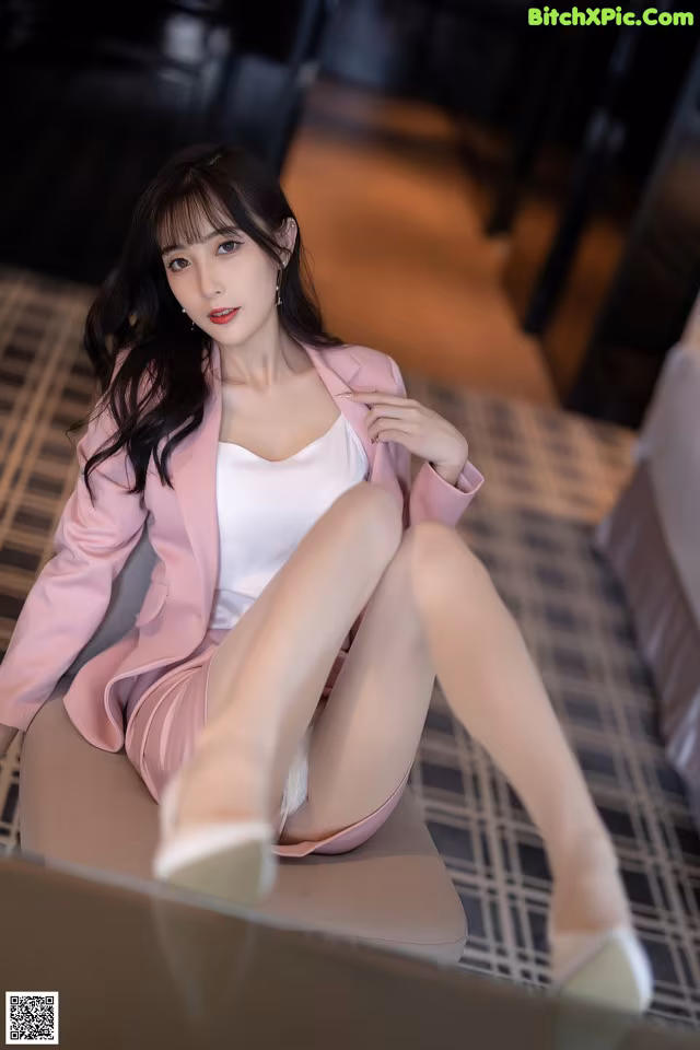 A woman in a pink suit sitting on a chair.