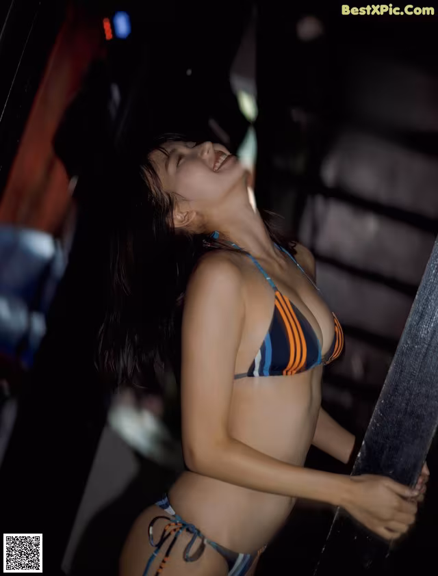 A woman in a bikini leaning against a pole.