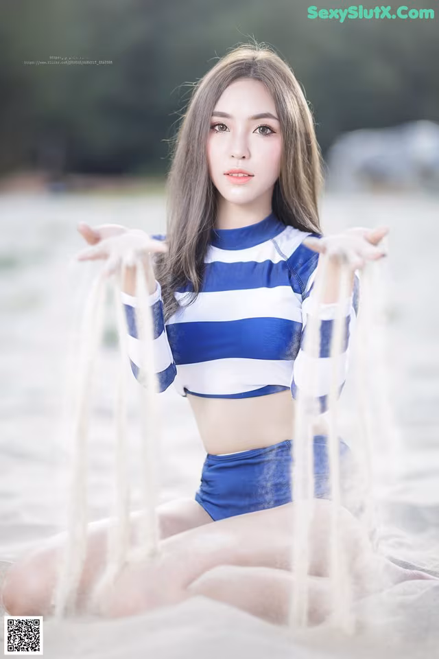 A woman in a blue and white striped top sitting on a beach.